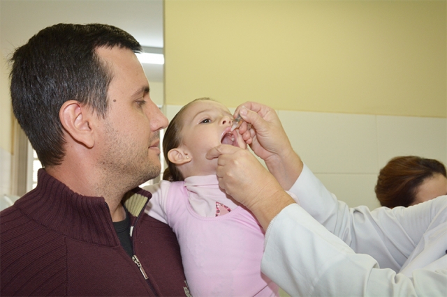 Pai leva a filha para receber a dose da vacina contra poliomielite